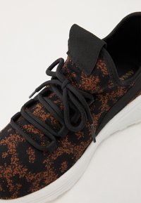 Fekete és narancs mintázatú sneaker, texturált kötött felső résszel, fekete fűzőkkel, párnázott nyelvvel és kontrasztos fehér gumi talppal.