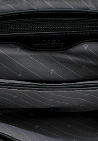 Interno di una borsa in pelle nera, con un rivestimento liscio e testurizzato caratterizzato da strisce diagonali e un logo. Chiusura con zip nella parte superiore.