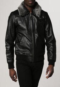 Schwarze Lederbomberjacke mit einem grauen Fellkragen, Reißverschluss vorne, seitlichen Taschen sowie gerippten Bündchen und Saum, die ein elegantes, strukturiertes Erscheinungsbild bieten.
