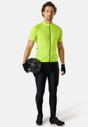 Maglia da ciclismo a maniche corte, di un vivace colore giallo, con zip, abbinata a pantaloni ciclistici neri. Il modello tiene un casco nero e indossa guanti senza dita.
