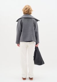 Grau Wollmantel mit weitem Kragen, kombiniert mit cremefarbenen Hosen und einer schwarzen Tasche, von hinten vor einem schlichten weißen Hintergrund gezeigt.