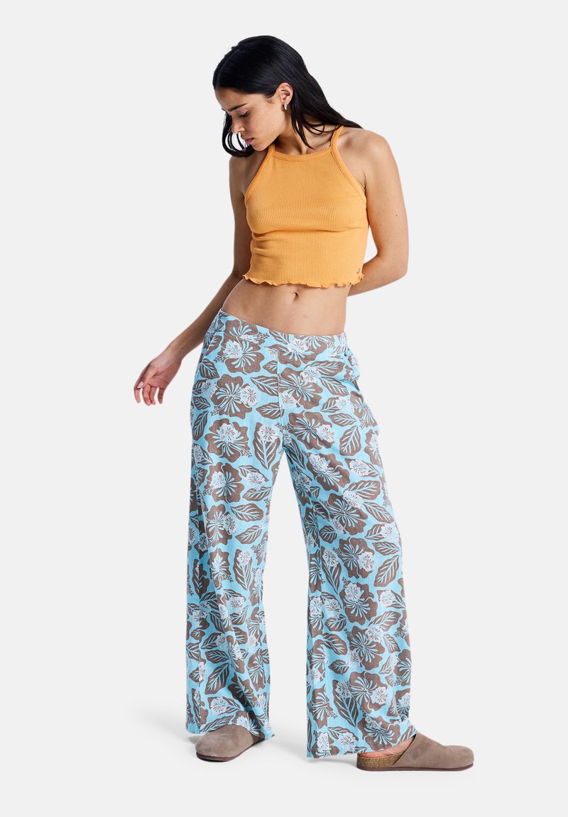 Crop top côtelé orange clair avec ourlet à volants, associé à un pantalon large bleu clair orné d'un motif floral marron et d'accents texturés.