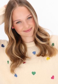 Beige sweater met kleurrijke hartpatronen in rood, groen, blauw en geel. Zachte textuur, medium breiwerk, ronde halslijn en lange mouwen.