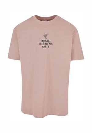 T-shirt rosa chiaro a maniche corte realizzata in un tessuto morbido, con una grafica nera che riporta la scritta "innocente fino a prova contraria" e un design di un uccello.