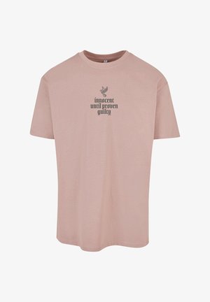 Világos rózsaszín, rövid ujjú póló, amely puha anyagból készült, fekete grafikával, rajta a "ártatlan, amíg be nem bizonyítják a bűnösségét" felirattal és egy madármintával.