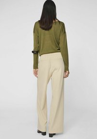 Beige wijde broek met een elastische tailleband, gecombineerd met een losvallend groen topje. Het materiaal lijkt zacht met een stevige textuur.