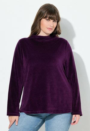 Maglione a collo alto in velluto viola con maniche lunghe, vestibilità morbida e texture soffice. L'orlo è dritto, abbinato a jeans in denim azzurro chiaro.