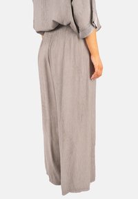 Pantalons légers gris avec une texture froissée et une coupe évasée. La taille élastique et les poches latérales offrent des détails fonctionnels.