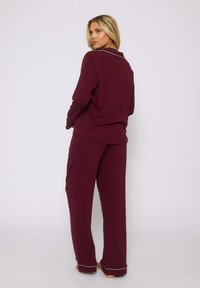 Set di abbigliamento da casa color bordeaux composto da una maglia a maniche lunghe con colletto e piping bianco a contrasto, abbinata a pantaloni larghi.