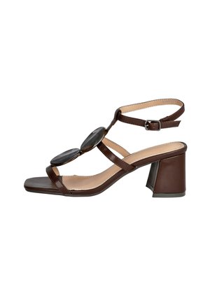 Sandalia de tacón bloque de cuero marrón con correa en el tobillo, dos grandes adornos ovalados decorativos y punta cuadrada abierta.