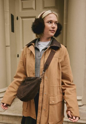 Brown canvas jacket with a dark collar, gray polo shirt, and brown crossbody purse. Black fur earmuffs add detail to the outfit.