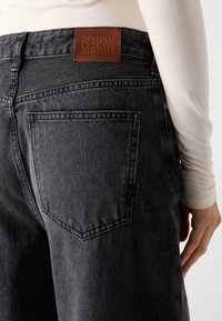 Zwarte denim jeans met een leren Scotch & Soda label, subtiele stikdetails en een klassiek zakontwerp. De textuur lijkt stevig.
