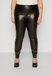 Black faux leather leggings with a slim fit, featuring a smooth texture, waistband, and tapered legs. Worn with black square-toed heels.