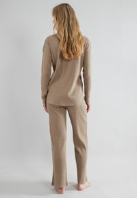 Beige geribde loungewear-set met een lange mouw top en bijpassende broek, met een ontspannen pasvorm en zijsplitten aan de onderrand.