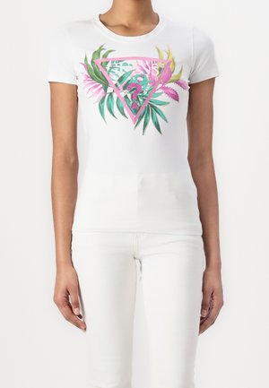 Femme portant un t-shirt blanc ajusté à manches courtes avec un motif de triangle rose, de feuilles tropicales vertes et roses, et de flamant rose.