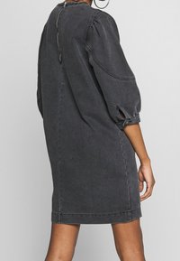 Mörkgrå denimklänning med puffärmar, hög krage och dragkedjestängning bak. Har en avslappnad passform och sidöppningar vid ärmsluten.