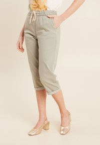 Pantalons courts vert clair avec une ceinture élastique et des ourlets roulés, associés à des chaussures à talons carrés dorées, mettant en valeur un design élégant.
