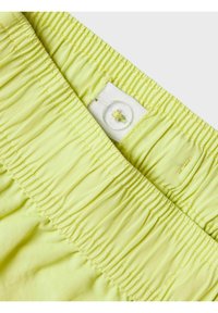 Heldere gele stoffen tailleband met geplooide textuur; beschikt over een wit etiket en knoopdetail. Zacht materiaal geschikt voor kleding.