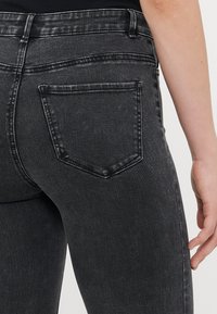 Nærbilde av en persons midje og hofte iført svarte denimjeans med en synlig baklomme og del av hånden deres.