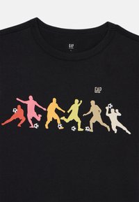 Sort bomulds t-shirt med farverige silhuetter af fodboldspillere i forskellige positurer med fodbold, samt et lille "GAP" logo øverst.