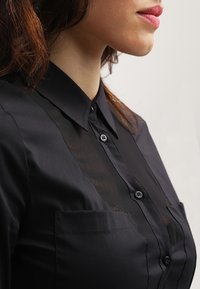 Czarna koszula zapinana na guziki z przezroczystą wstawką, klasycznym kołnierzykiem i dwiema przednimi kieszeniami. Gładka faktura i dopasowany krój.