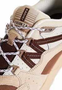 Sneaker con sopra in suede crema e marrone, pannelli in mesh e lacci intrecciati. Presenta una linguetta imbottita con etichetta "Karhu Fusion 2.0".
