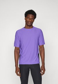 Camiseta deportiva de manga corta en color púrpura con cuello redondo, fabricada en un tejido ligero. Presenta un corte holgado y detalles de costura sutiles.
