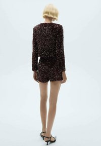 Body con in raso bordeaux con maniche lunghe e pantaloncini, decorato con numerosi paillettes luccicanti, abbinato a tacchi neri.
