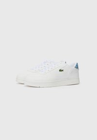 Sneaker in pelle bianca con suola piatta, punta rotonda e chiusura con lacci. Presenta un logo di coccodrillo verde e accenti blu sul tallone.