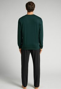 Groene langesleeve shirt met een ronde hals, gecombineerd met zwarte broeken. Gladde stof, eenvoudig ontwerp en geen zichtbare patronen of details.