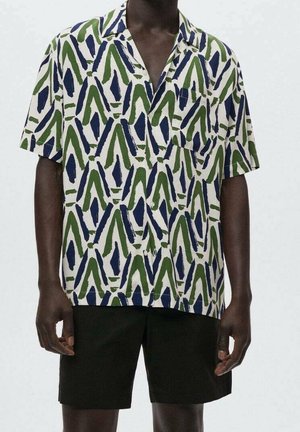 Man wearing short-sleeve button-up shirt with green and blue abstract pattern and black shorts, standing against a plain light background.