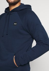 Felpa blu navy in tessuto morbido, con tasca frontale, polsini a costine e un piccolo logo nero sulla parte superiore del petto.