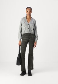 Grå strikket cropped cardigan med kabelstrikkmønster, med fire svarte knapper. Kombinert med mørkegrønne cordurypants med vide ben og svarte sko.
