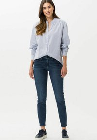 Chemise à rayures bleu clair avec un col mandarin, associée à un jean ajusté bleu foncé et des baskets navy.