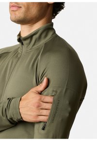 Olivgrüne Zip-Jacke mit hohem Kragen, aus glattem, dehnbarem Material gefertigt. Verfügt über eine Reißverschlusstasche am linken Ärmel.