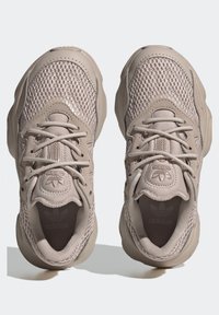 Beige atletiska sneakers med nät- och syntetmaterial, rundad tå, snörning och texturerad sula. Har Adidas-logotyp på tungan.