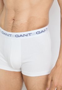 Boxers blancs en coton avec une ceinture élastique de marque bleu marine, présentant un design ajusté et une texture lisse.
