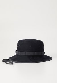 Chapeau seau noir en nylon, avec une large bordure, une bande en tissu et un cordon de serrage ajustable. Texture lisse avec des œillets renforcés.