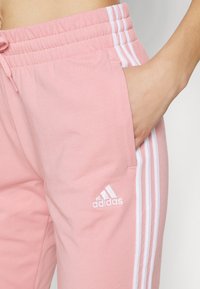 Rosa Baumwoll-Sweatpants mit elastischem Taillenbund, weißen drei Streifen an den Seiten und einem gestickten weißen Adidas-Logo.