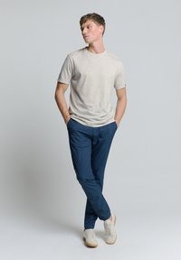 Lichtgrijze T-shirt met korte mouwen gecombineerd met marineblauwe broek, met een relaxte pasvorm. Model draagt crèmekleurige sneakers. Over het geheel een soepele textuur.