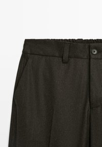 Dark gray trousers with elastic back waistband, front button closure, belt loops, and side pockets, shown from the waist down.