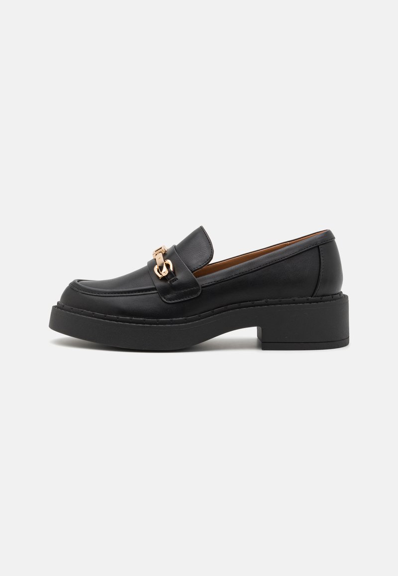Schwarze Lederloafers mit einer klobigen Plateausohle, die einen auffälligen goldenen Hardwareakzent auf dem Blatt sowie sichtbare Nähdetails aufweisen.