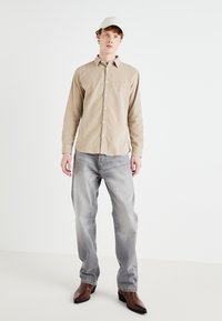 Beige corduroy shirt with button front and long sleeves, paired with light gray jeans and brown leather boots, topped with a white cap.