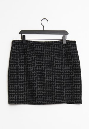 Jupe à motifs noir et gris avec un tissu texturé, présentant une coupe droite et une taille, suspendue à un cintre en plastique noir.