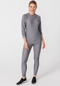 Camiseta atlética de manga larga gris con mangas raglán, combinada con leggings a juego hechos de una tela texturizada. Zapatillas atléticas negras completan el conjunto.