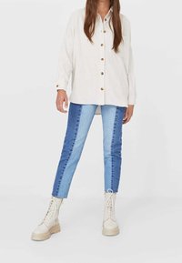 Beige corduroy shirt with wooden buttons, paired with color-blocked blue denim jeans. Cream lace-up boots complete the outfit.