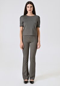 Top corto a motivi a scacchi monocromatici con maniche a sbuffo corte, abbinato a pantaloni sartoriali coordinati. Il tessuto appare liscio con una leggera lucentezza.
