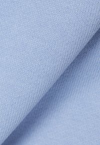Tissu tricoté bleu clair montrant une texture en gros plan et un motif de point fin avec un léger pli sur la surface.