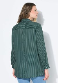 Blusa verde a righe con maniche lunghe, dotata di colletto classico, polsini abbottonati e placca con bottoni sul retro. Tessuto morbido.