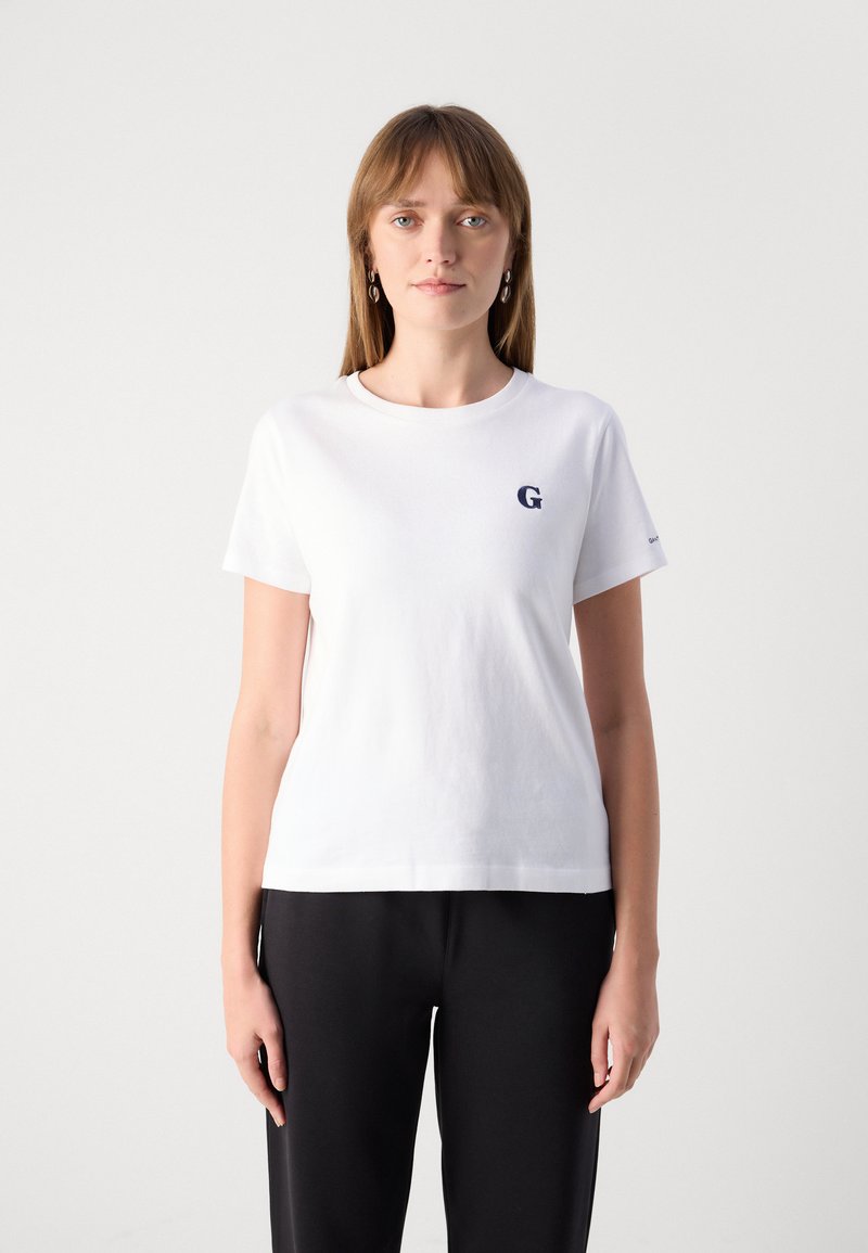 Weißes Baumwoll-T-Shirt mit rundem Halsausschnitt, kurzen Ärmeln und einem gestickten marineblauen "G"-Logo auf der linken Brustseite. Schlichtes Design, weiche Textur.